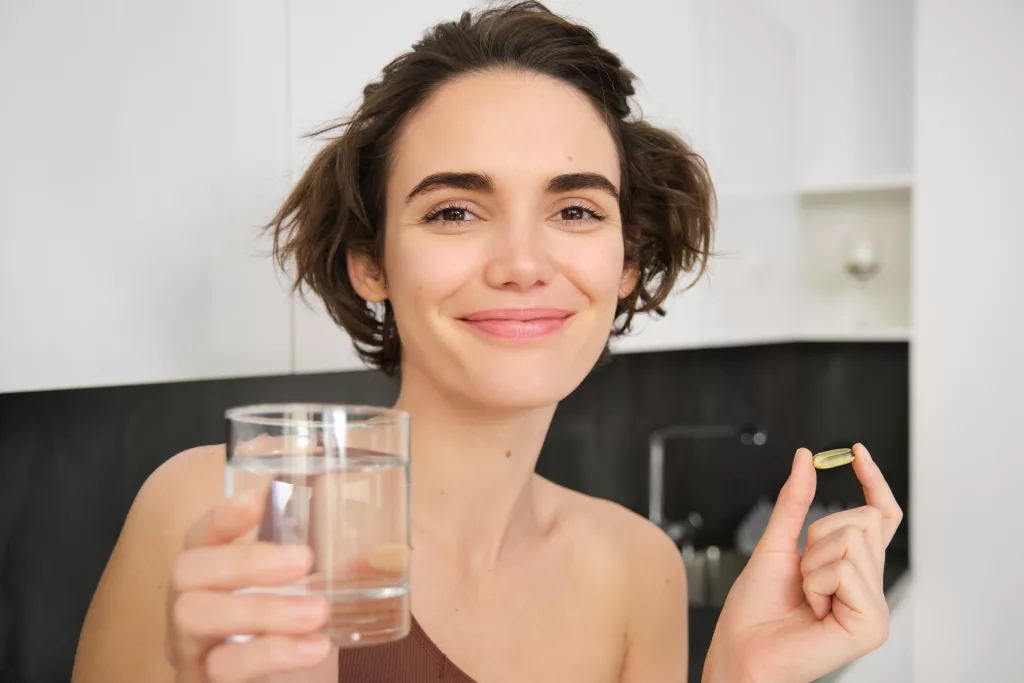 Młoda kobieta przyjmująca witaminę C, D omega-3 ze szklanką wody